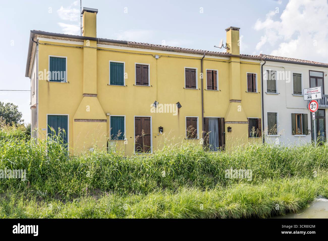 Paesaggio urbano con case tradizionali con camini esterni sulla riva del canale di Brenta, girato con la luce estiva a Oriago, Veneto, Italia Foto Stock