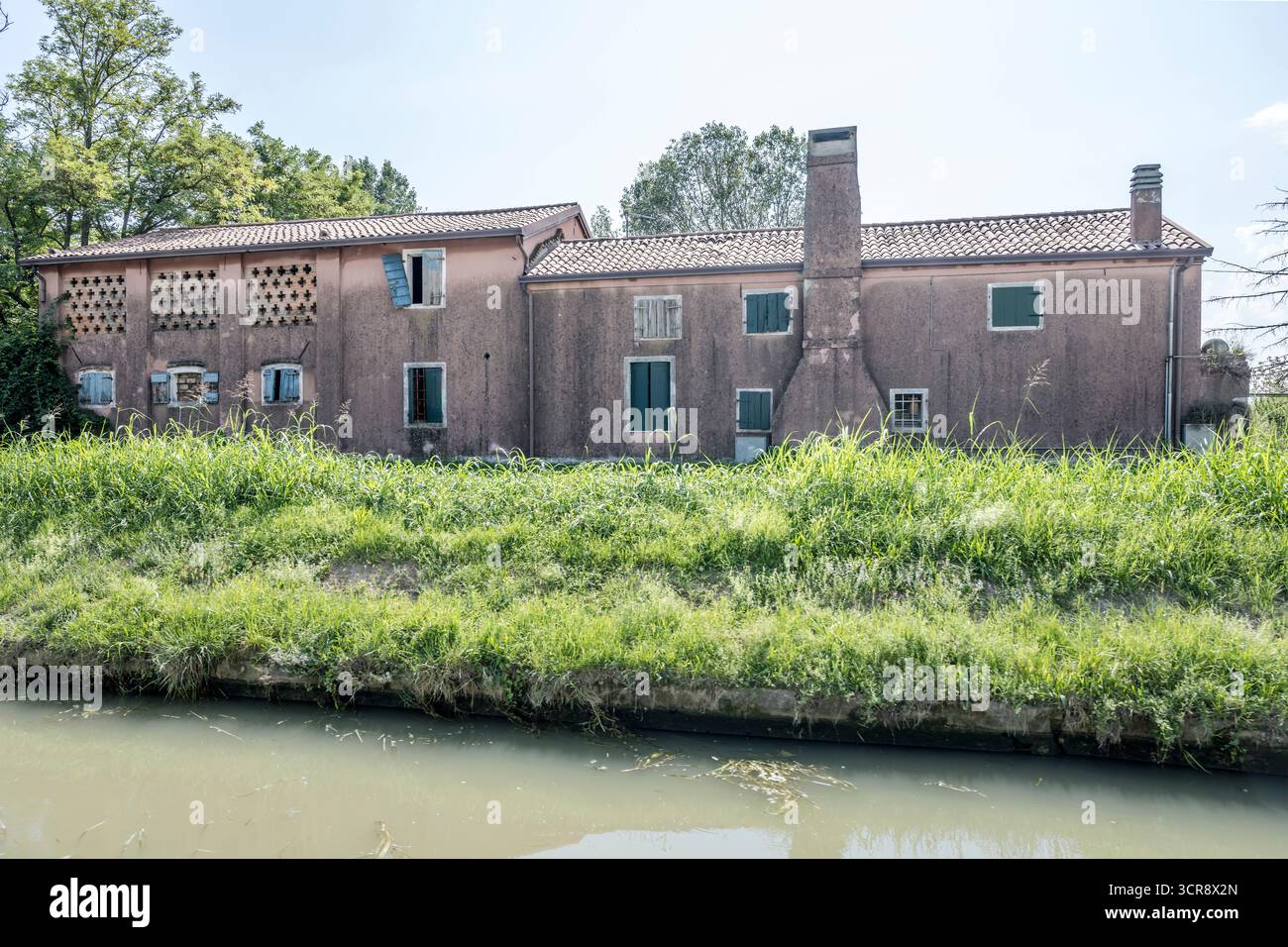 Paesaggio urbano con case tradizionali sbriciolate con camini esterni sulla riva del canale di Brenta, girato con la luce estiva a Oriago, Veneto, Italia Foto Stock