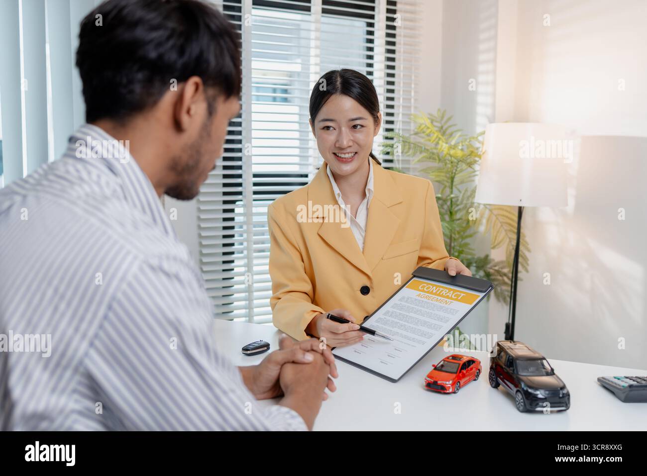 Una negoziazione per la vendita di auto si svolge in un ufficio in cui una donna venditrice con un blazer giallo spiega i dettagli di un contratto a un cliente maschio, showin Foto Stock