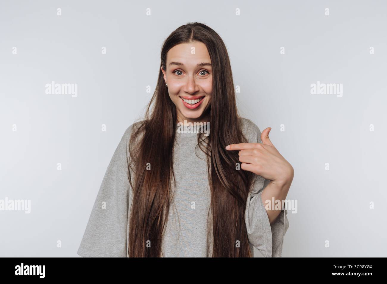 Una giovane donna posa giocosamente su uno sfondo semplice, mostrando i suoi lunghi capelli e la sua espressione allegra durante un momento informale Foto Stock Una giovane donna posa giocosamente su uno sfondo semplice, mostrando i suoi lunghi capelli e la sua espressione allegra durante un momento informale Foto Stock