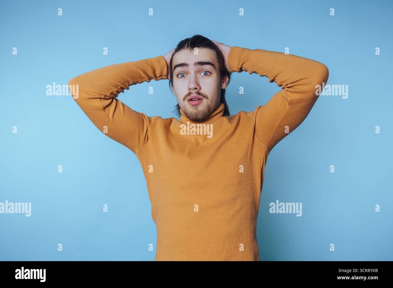 Giovane uomo che esprime sorpresa davanti a uno sfondo azzurro durante un momento informale Foto Stock Giovane uomo che esprime sorpresa davanti a uno sfondo azzurro durante un momento informale Foto Stock