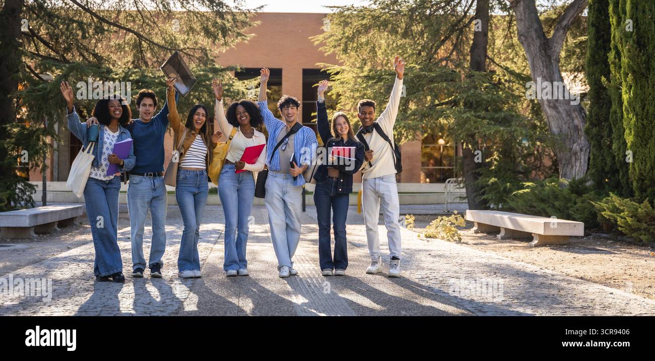 Gruppo di giovani, felici e diversi studenti universitari che si uniscono, alzando le mani per celebrare il successo accademico e l'amicizia all'università Foto Stock