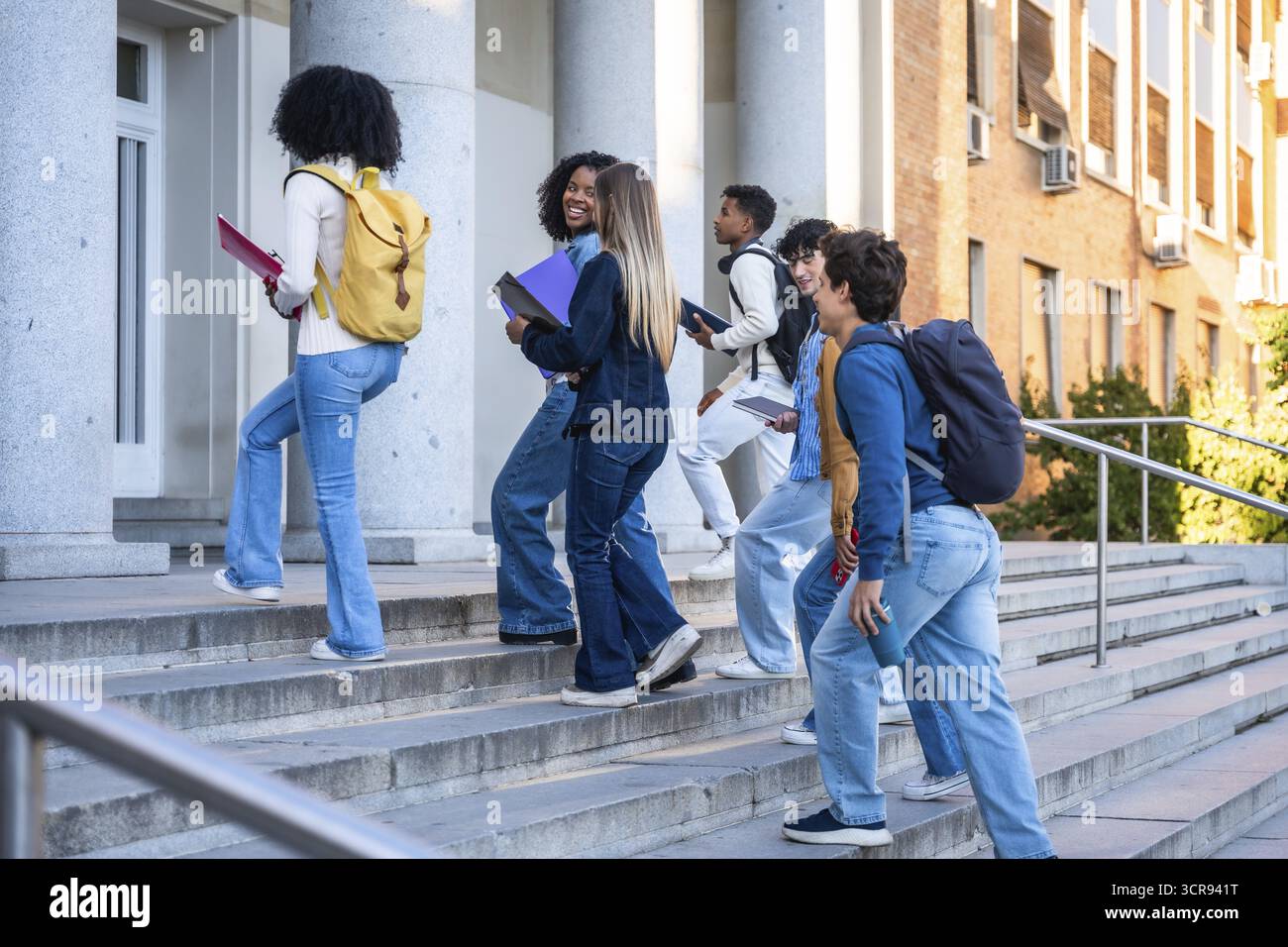 Diversi gruppi di studenti universitari salgono le scale del campus con zaini e libri, godendosi la giornata di sole, il lavoro di squadra e l'ambizione mentre si dirigono verso l'hig Foto Stock