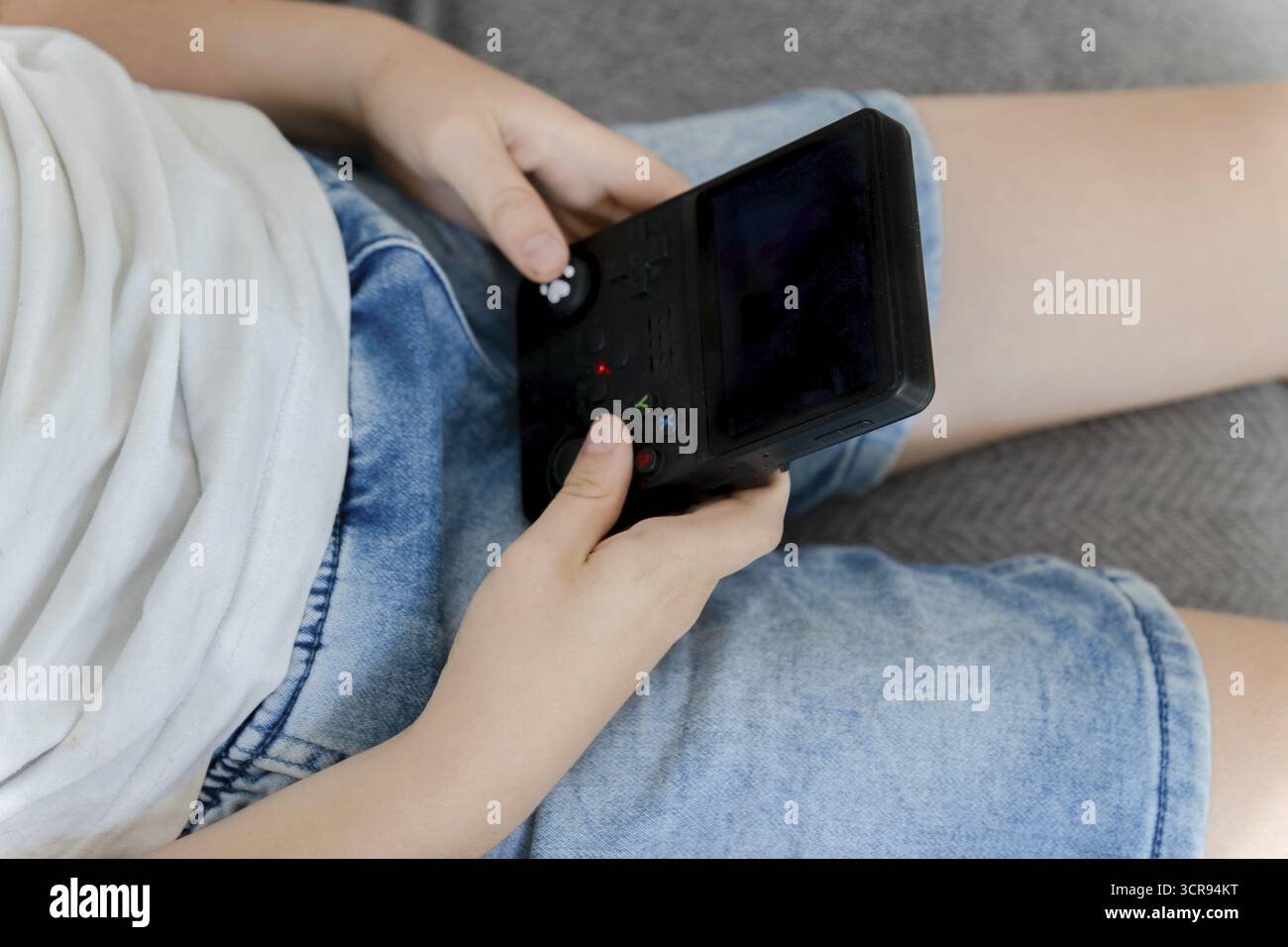 Il bambino tiene le mani e gioca con la console portatile per videogiochi durante il tempo libero Foto Stock