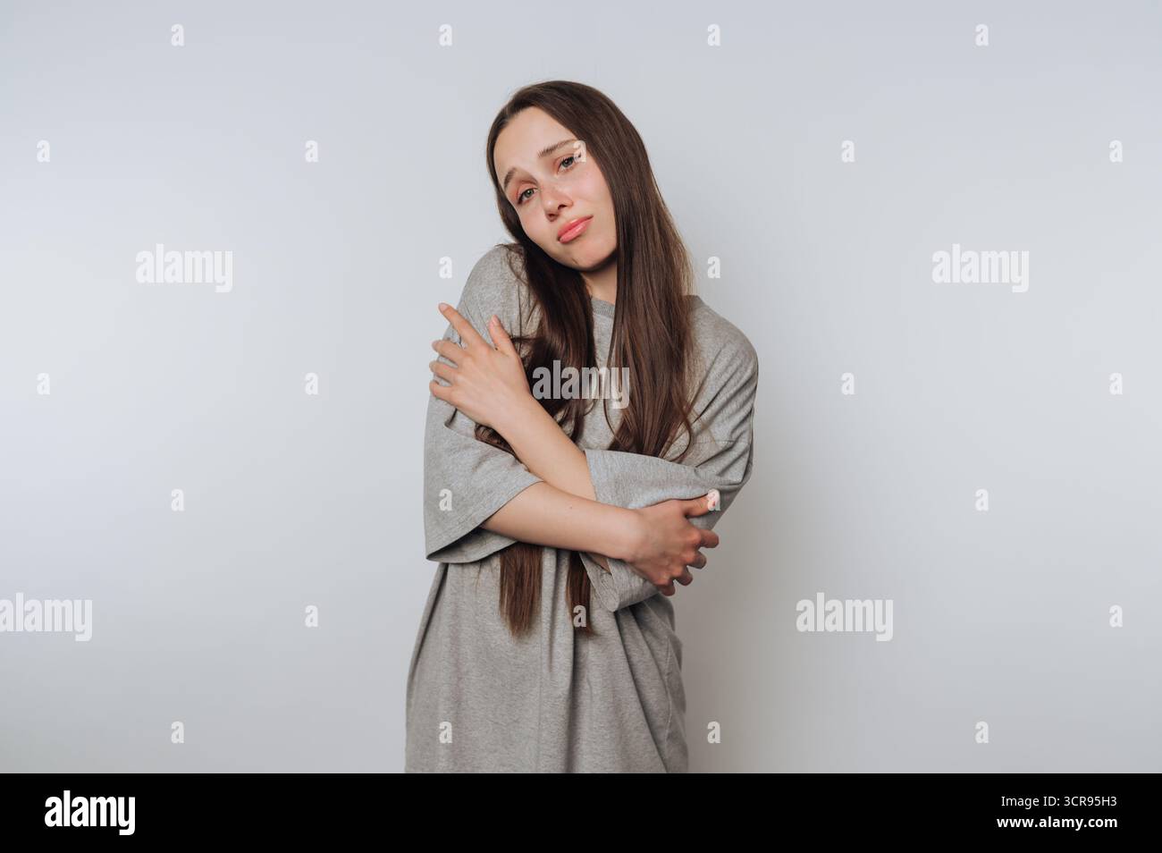 la giovane donna pensiva si trova in una posa premurosa, incarnando la vulnerabilità su sfondo bianco Foto Stock