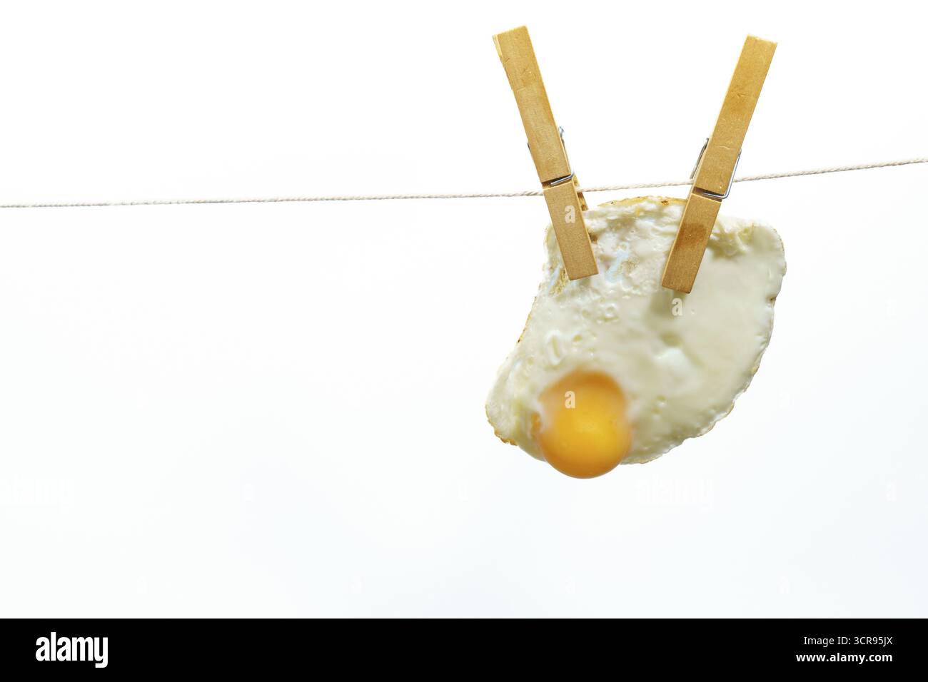 Clothespins che reggono l'uovo fritto sulla clothesline su sfondo bianco, creando un'immagine stravagante e insolita Foto Stock