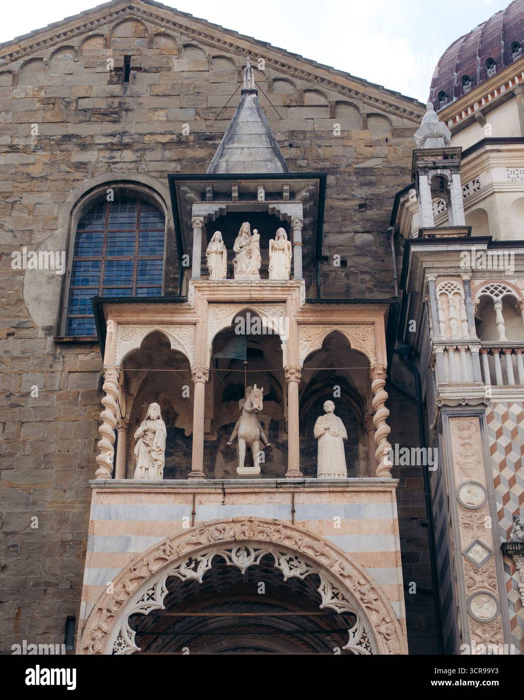 La vista di intricate pietre e statue bianche adornano la facciata di un edificio storico, inondata dalla luce soffusa del giorno, che mostra la bellezza architettonica di Bergamo, Lombardia, Italia. Foto Stock
