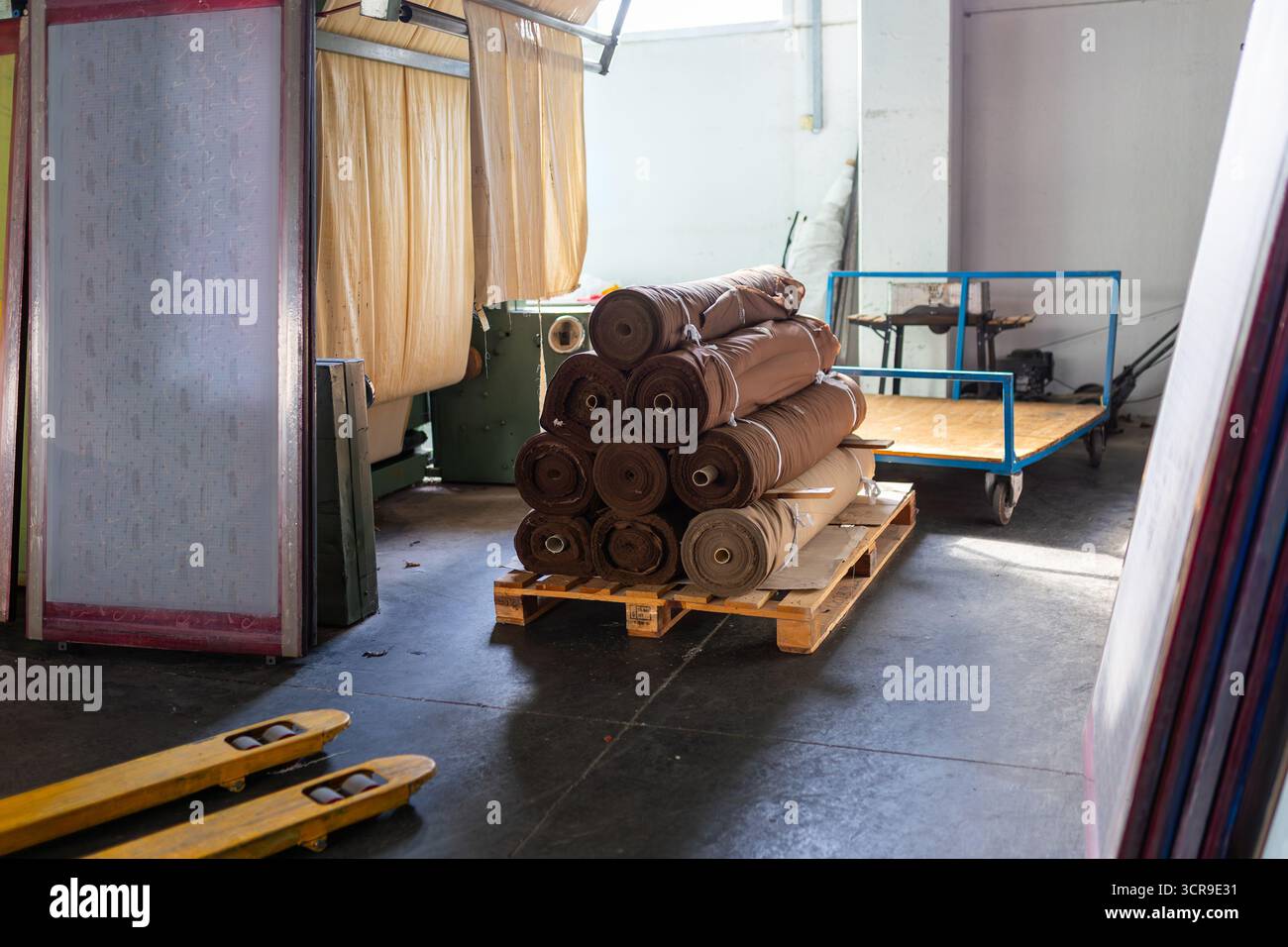 Magazzino tessile/serigrafia. Rotoli di tessuto su pallet, telai per serigrafia, industria, stoccaggio e produzione artigianale. Foto Stock