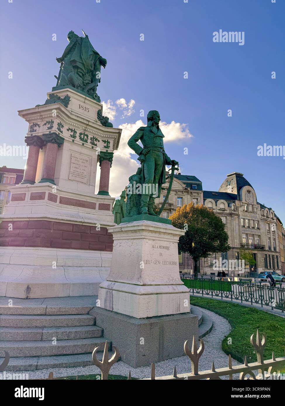Vista frontale del Monumento Lecourbe a Belfort, Francia, con statue in bronzo e un piedistallo in pietra neoclassico sotto un cielo azzurro - Immagine stock catturata con smartphone