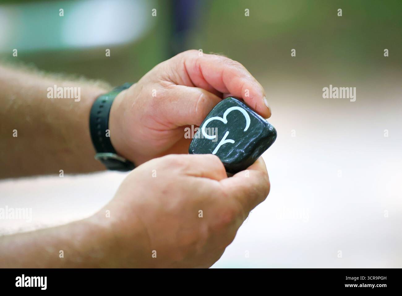 Primo piano di una persona che regge una roccia nera con un simbolo di eventi di parkrun scolpiti su di essa Foto Stock