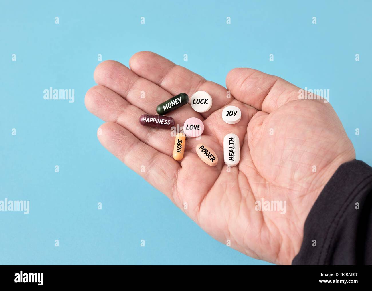 Mano aperta che mostra pillole colorate etichettate con concetti come denaro, amore e salute, simboleggiando la cura per raggiungere gli obiettivi della vita e la felicità Foto Stock