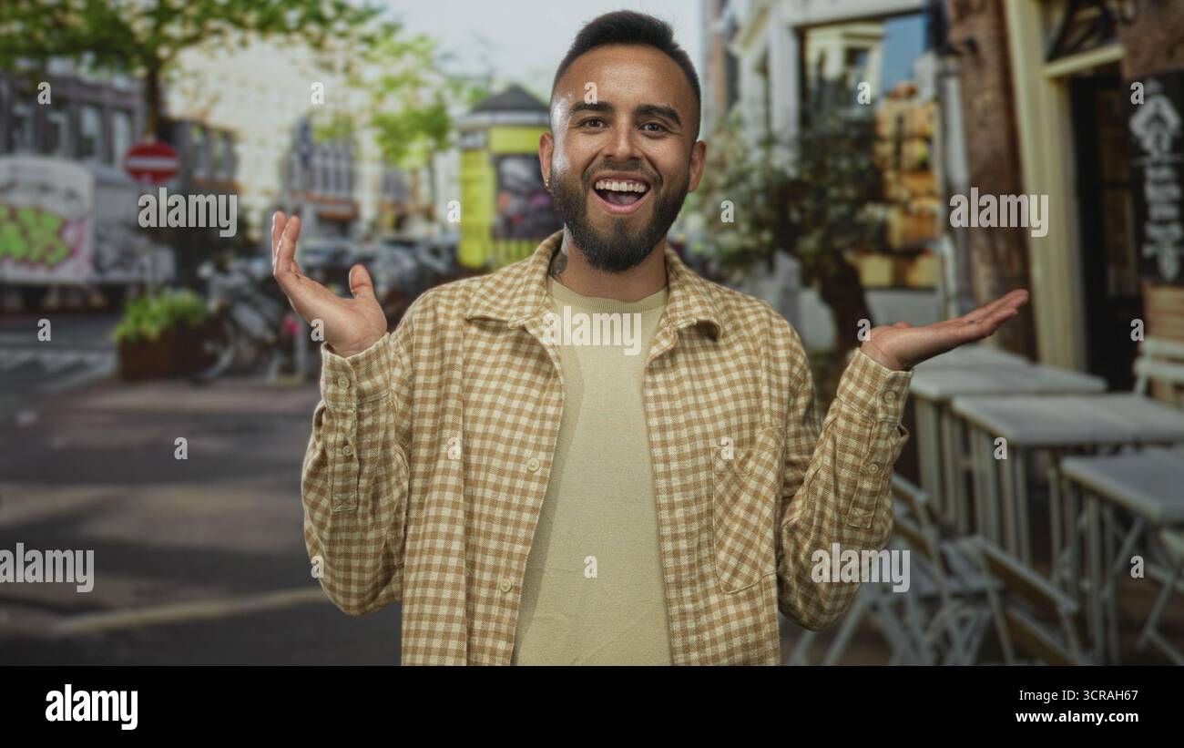 Uomo con una camicia e una camicia a quadri sorridente con palme aperte e leggermente appoggiato in avanti su una strada trafficata della città fiancheggiata da tavoli da caffe'; gioia guerra di cordialità Foto Stock