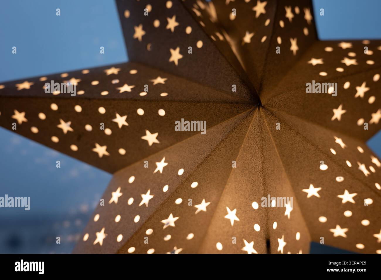 Una lanterna a stella di carta brillante con ritagli decorativi di stelle e punti che irradiano una luce calda. Perfetto per Natale, Capodanno, stagione dell'avvento e per il resto Foto Stock