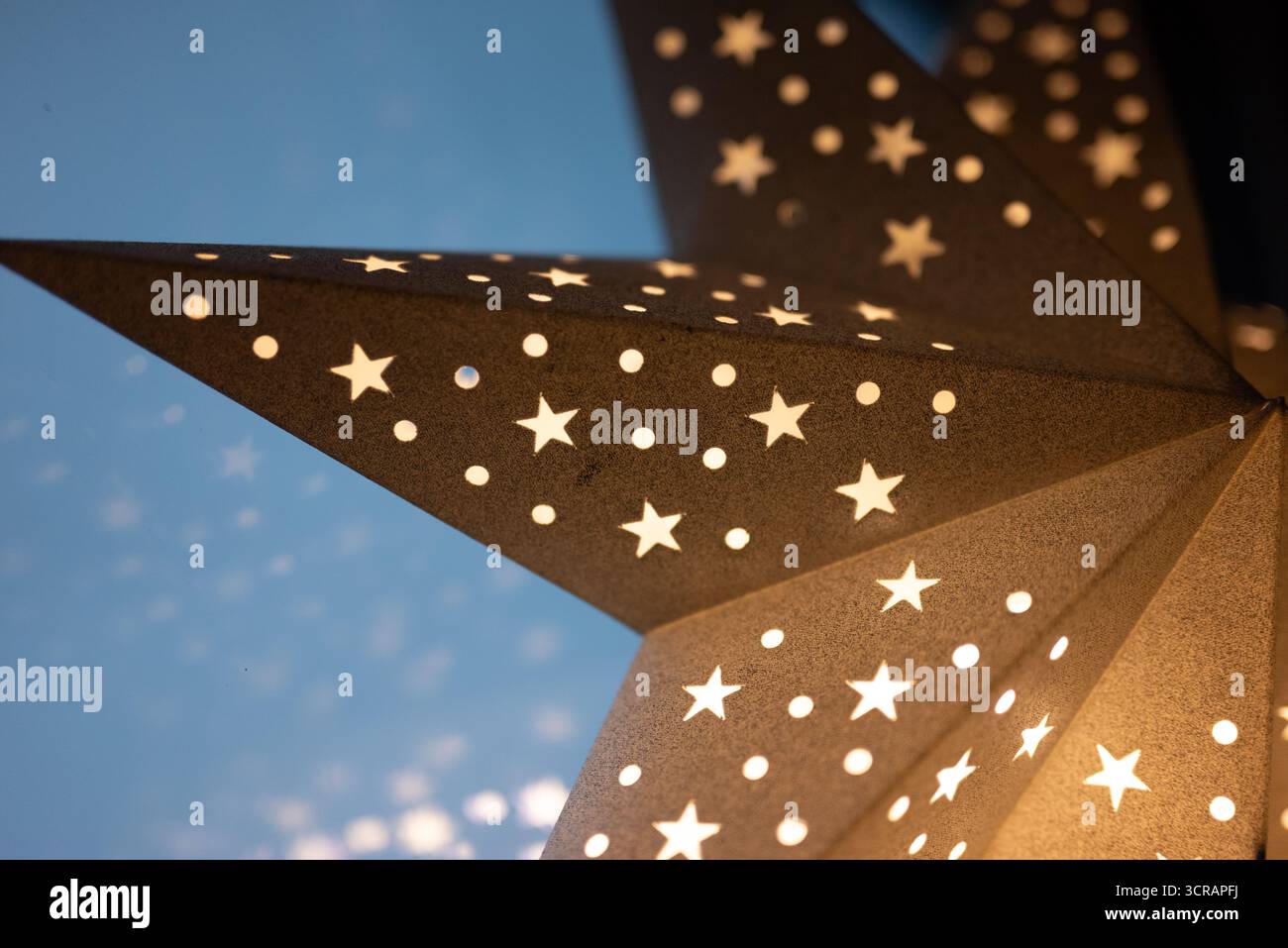 Primo piano di una lanterna a stella di carta brillante con motivi a stella e punti ritagliati, che brillano calorosamente su uno sfondo morbido. Ideale per Natale e inverno Foto Stock