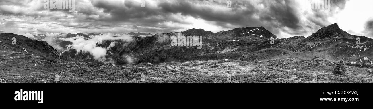 Panorama monocromatico grandangolare che raffigura montagne aspre e nuvole dinamiche contro un cielo spettacolare. Foto Stock
