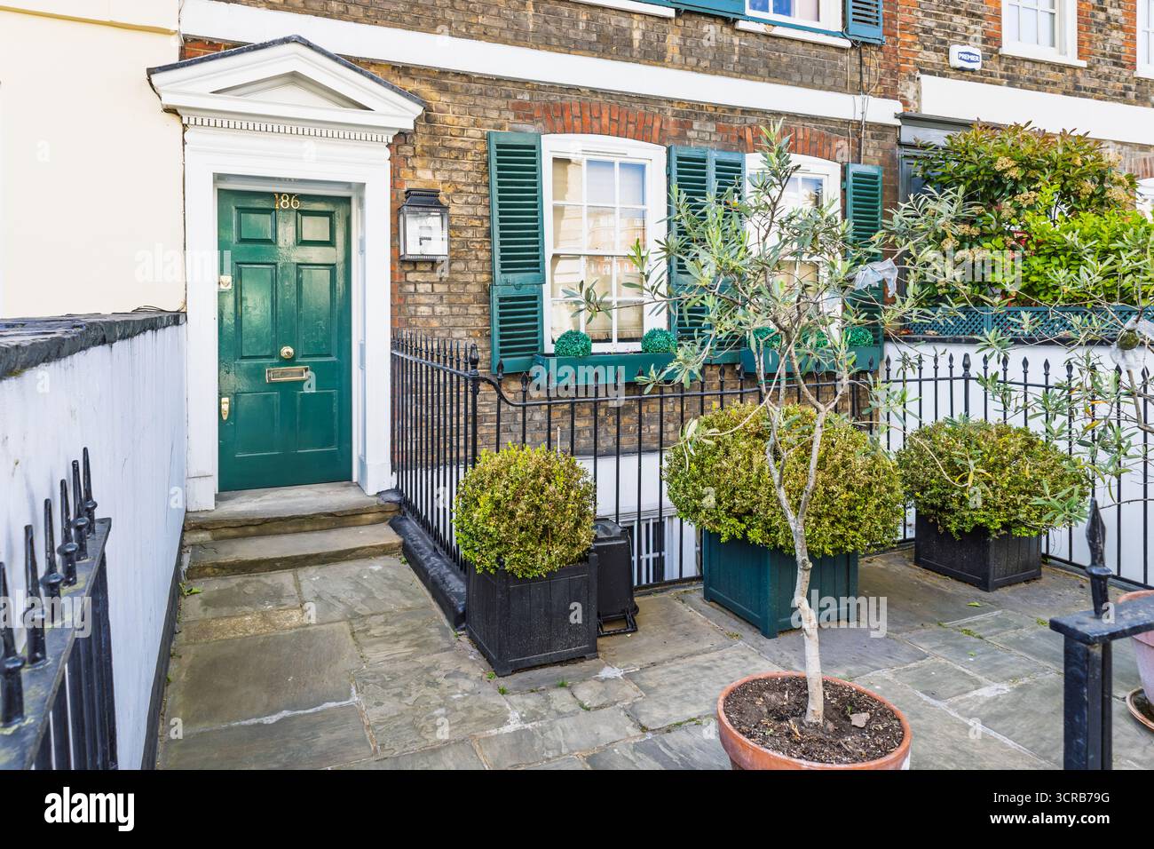 Classica entrata della casa cittadina di Londra con porta verde, facciata in mattoni e topiario in vaso Foto Stock