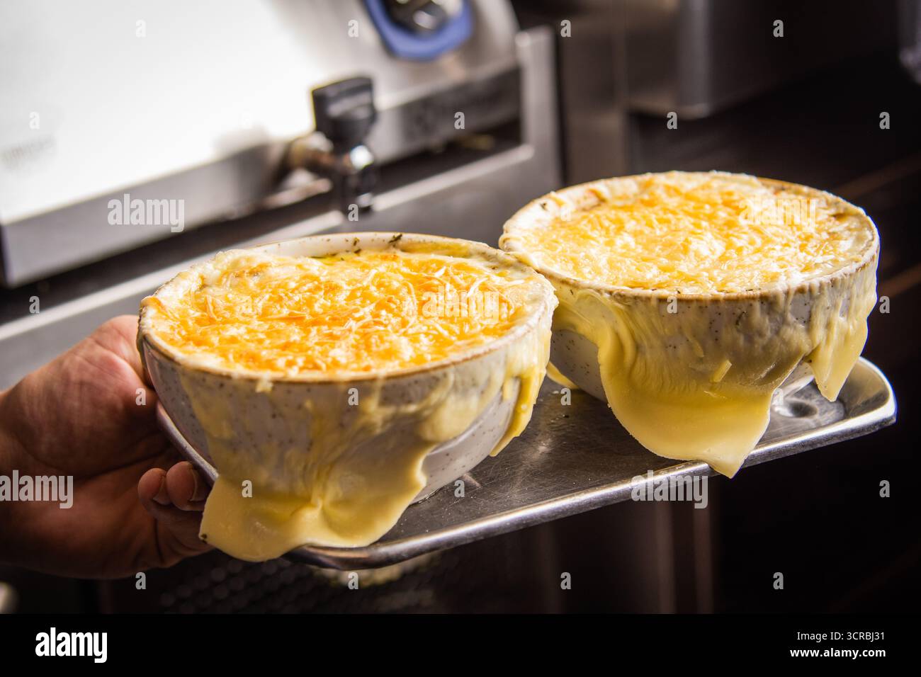 Viziatevi con i sapori ricchi e confortevoli della classica zuppa di cipolle francese, condita con una cascata di formaggio Gruyère marrone dorato perfettamente fuso. Foto Stock