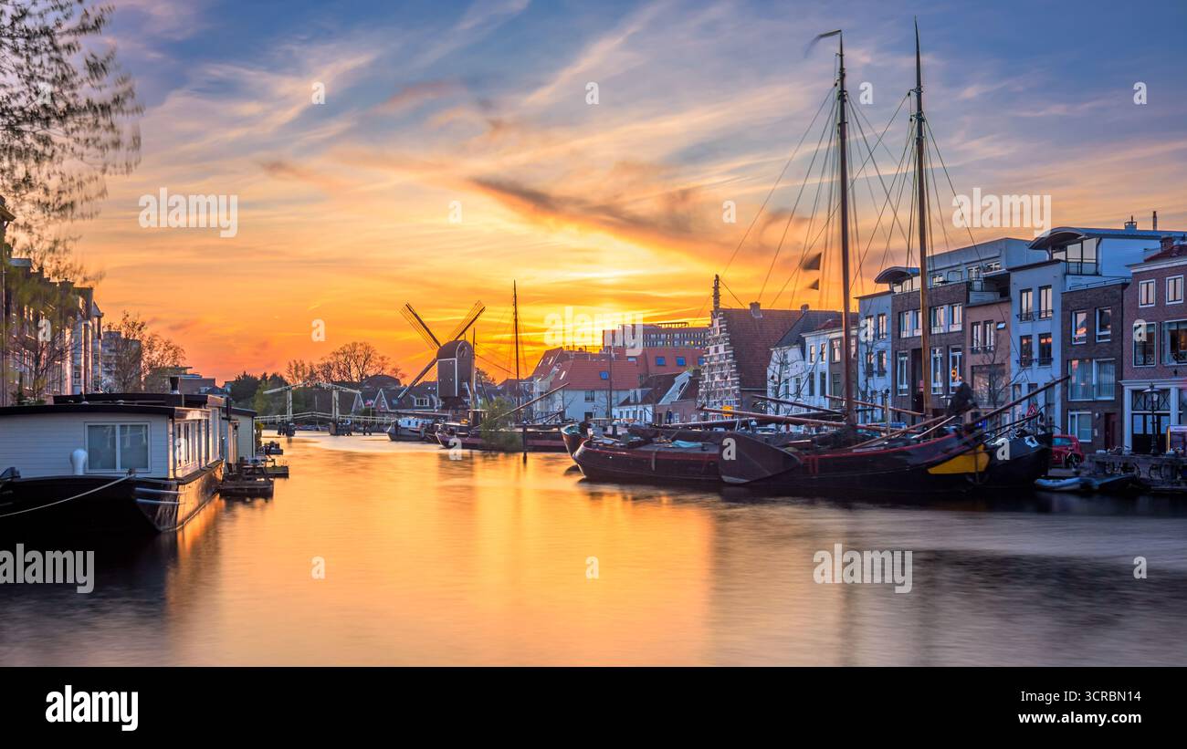 Splendido tramonto sui canali di Leida, Paesi Bassi. Canale Korte Galgewater con vecchie navi e mulino Foto Stock