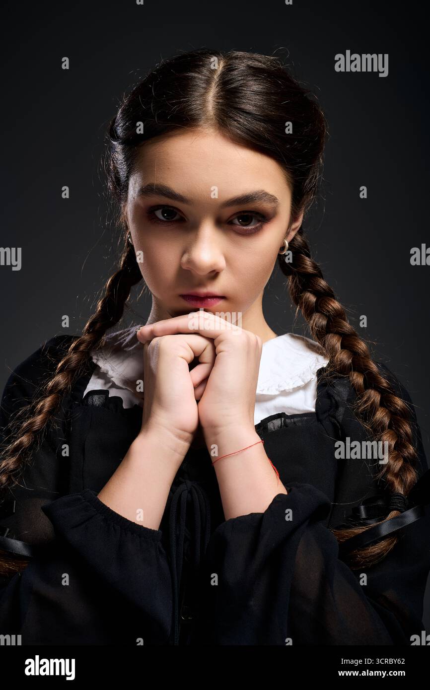 Una ragazza con trecce indossa un abito gotico, catturando l'essenza di un personaggio del mercoledì di Halloween. Foto Stock