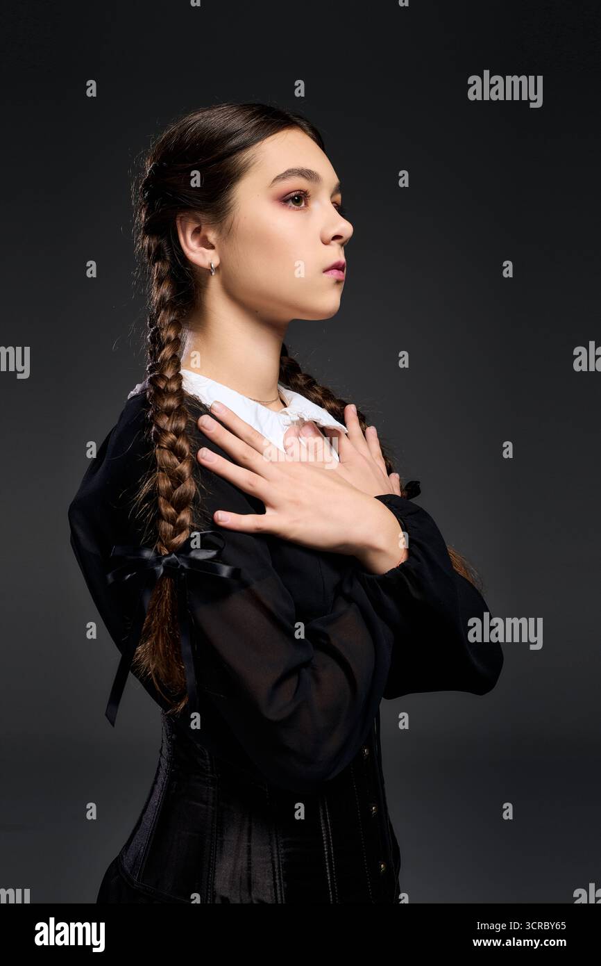 Una ragazza in treccia indossa un abito gotico, fingendosi un personaggio serio del mercoledì. Foto Stock