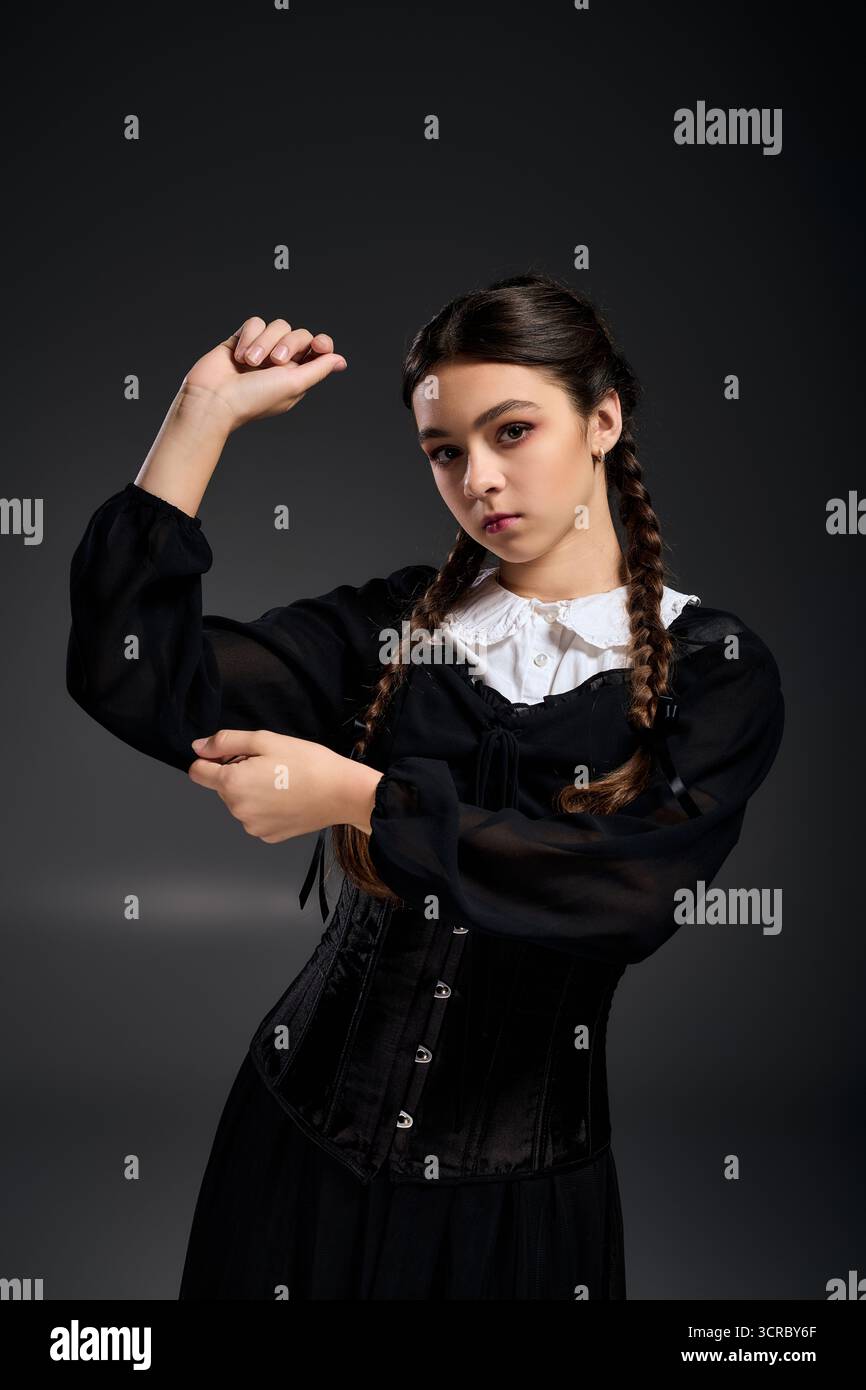 Una ragazza in treccia indossa un abito gotico del mercoledì, che incarna un personaggio di Halloween in una scena spaventosa. Foto Stock