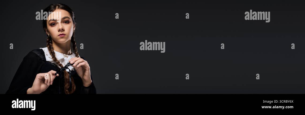 La ragazza con trecce indossa un abito in stile gotico del mercoledì ispirato a un personaggio spaventoso amato, uno striscione Foto Stock