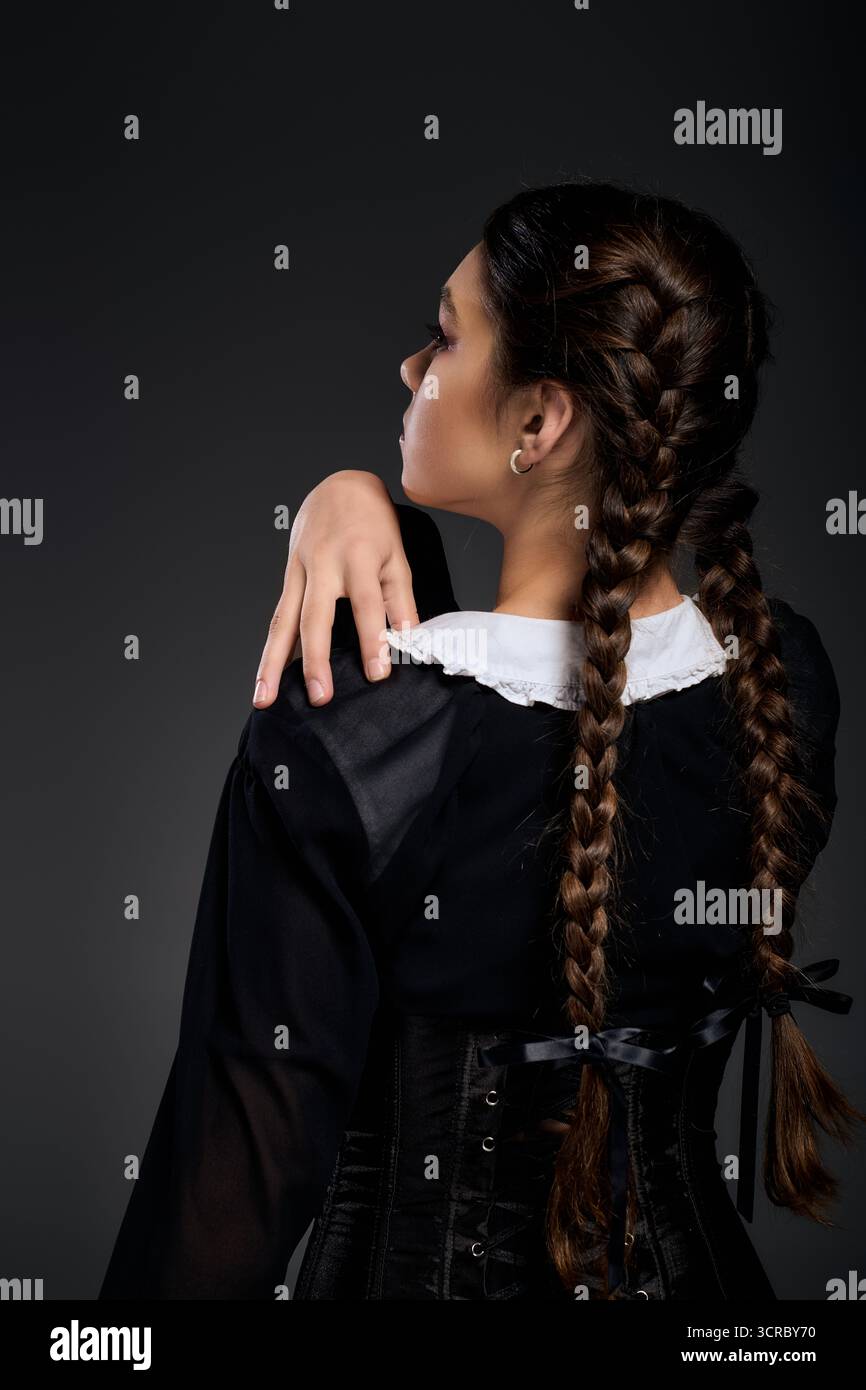 Una ragazza con trecce in un abito gotico del mercoledì con mano sulla spalla Foto Stock