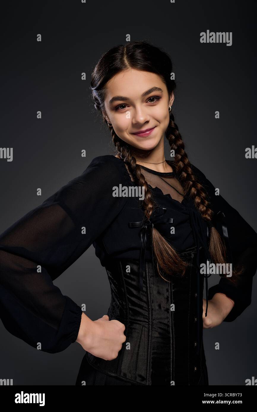 Una ragazza con trecce indossa un abito gotico mercoledì e sorride mentre celebra Halloween. Foto Stock