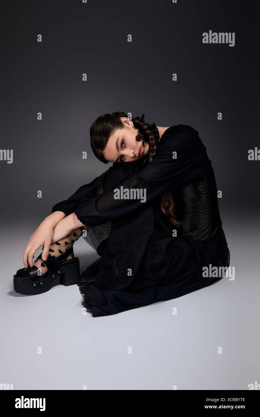 Un bambino con trecce seduto con grazia in un abito scuro del mercoledì, catturando l'essenza di Halloween. Foto Stock