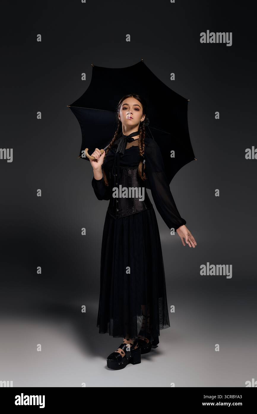 Una ragazza ispirata al mercoledì in un abito gotico si posa con un ombrello, incarnando lo spirito di Halloween in ottobre. Foto Stock