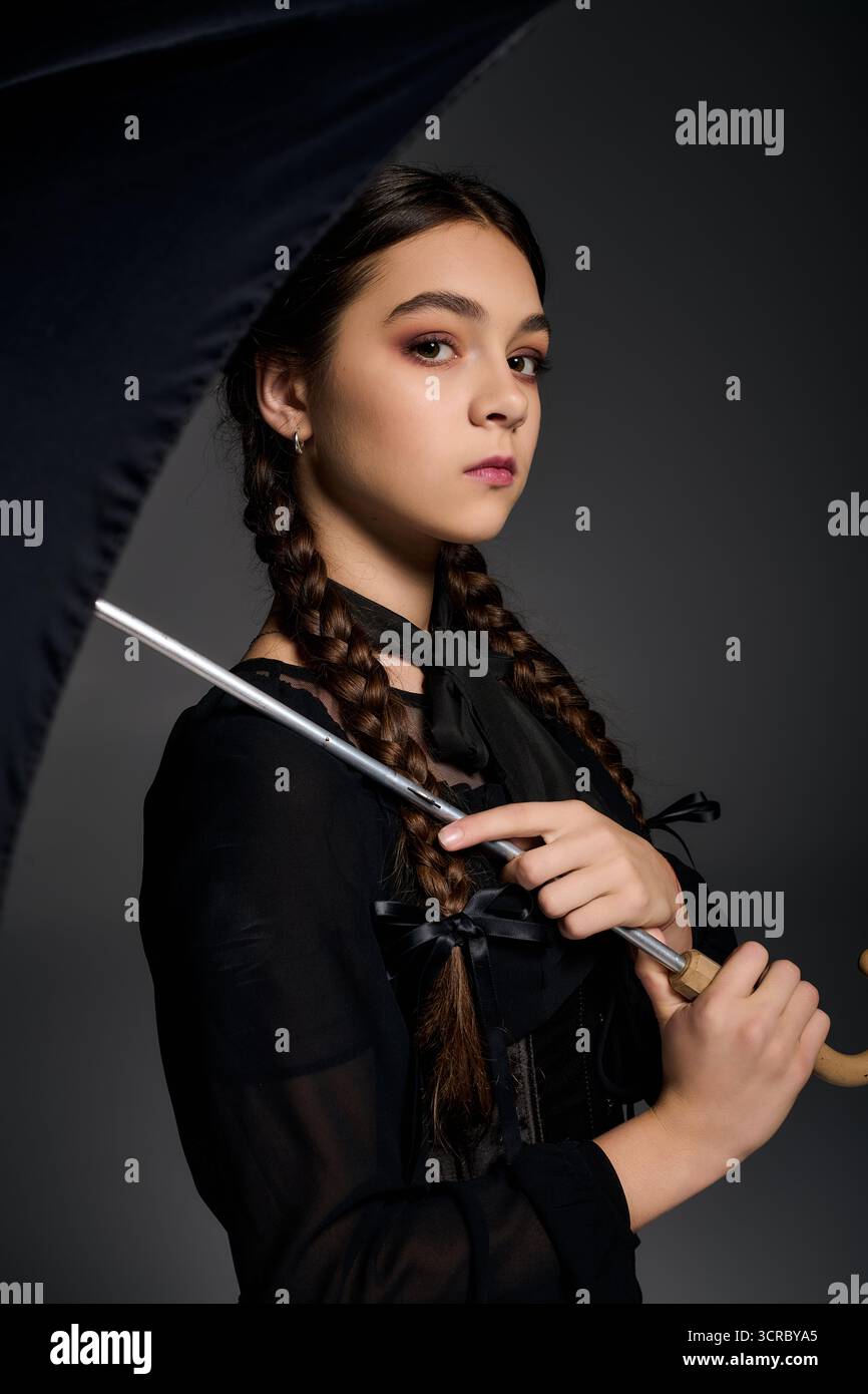 Una ragazza con trecce si posa in un abito gotico del mercoledì, incarnando lo spirito di Halloween con eleganza. Foto Stock