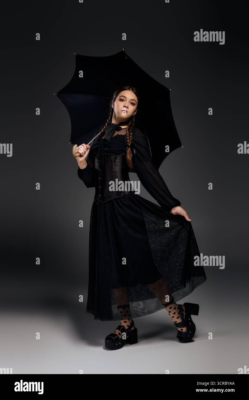 Una ragazza con trecce indossa elegantemente un abito gotico, catturando in modo splendido lo spirito di Halloween. Foto Stock