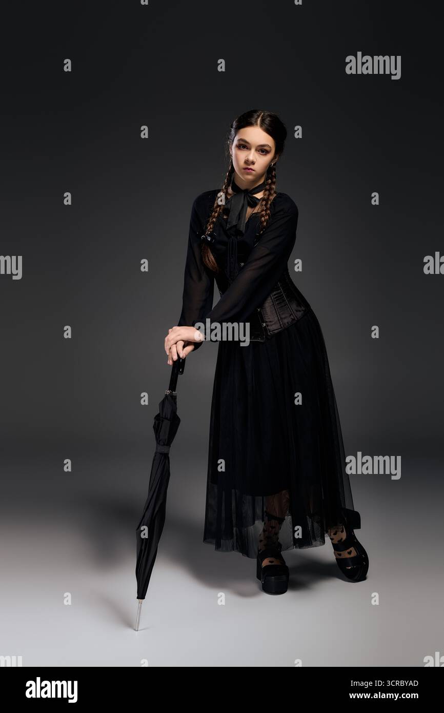 Una ragazza con un abito nero del mercoledì con trecce pose con un ombrello, per celebrare Halloween Foto Stock