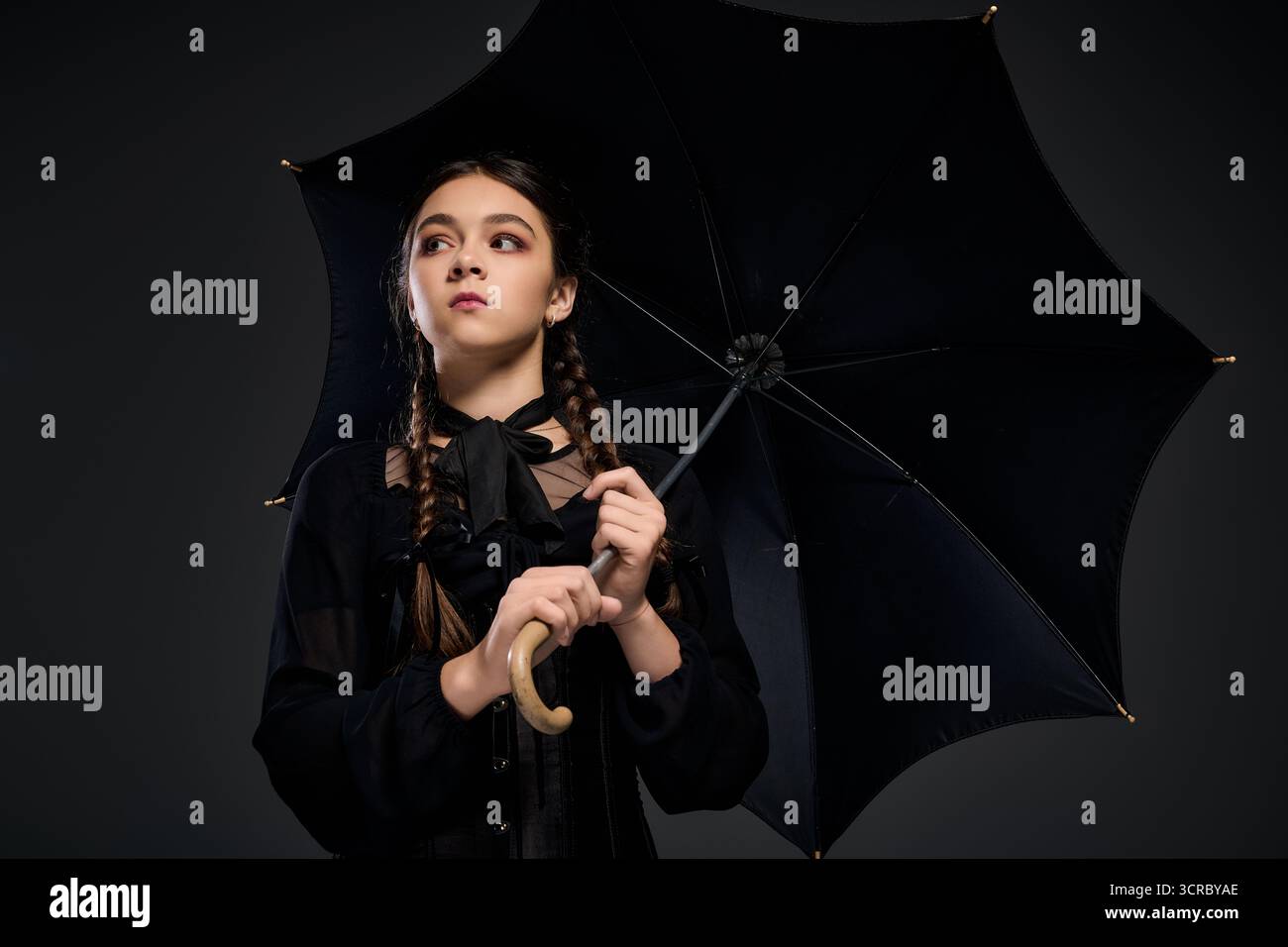 Una ragazza con un abito e trecce del mercoledì porta un ombrello nero che abbraccia Halloween. Foto Stock