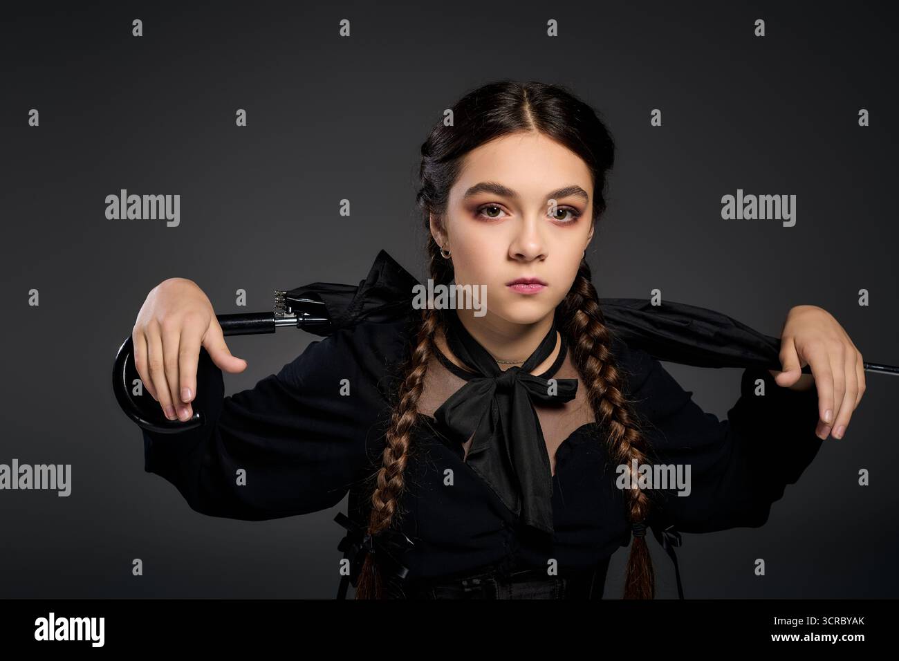 Una ragazza con trecce indossa un costume del mercoledì ispirato a Halloween, che esprime un fascino spettrale. Foto Stock