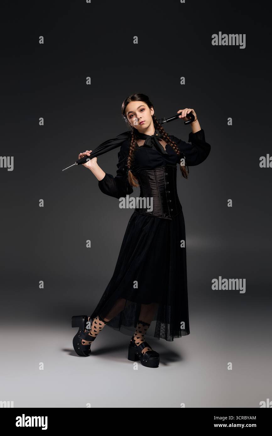 Una ragazza con le trecce è vestita con un costume gotico del mercoledì, canalizzando un'atmosfera spettrale. Foto Stock