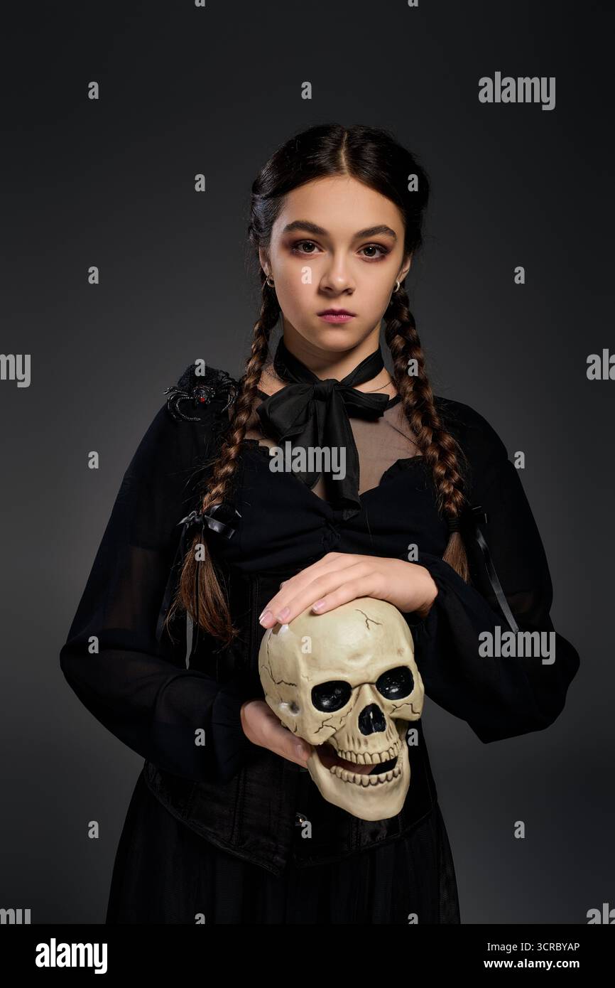 Una ragazza con trecce vestita in stile gotico mercoledì posa con un teschio per Halloween. Foto Stock