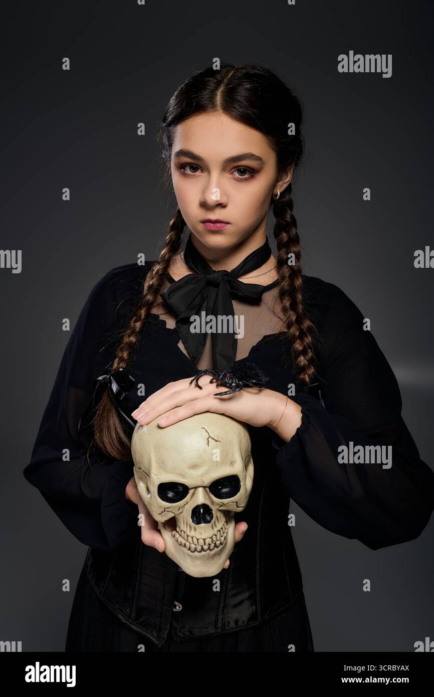 Una ragazza con un abito gotico ha un teschio, catturando lo spirito di Halloween e mercoledì. Foto Stock