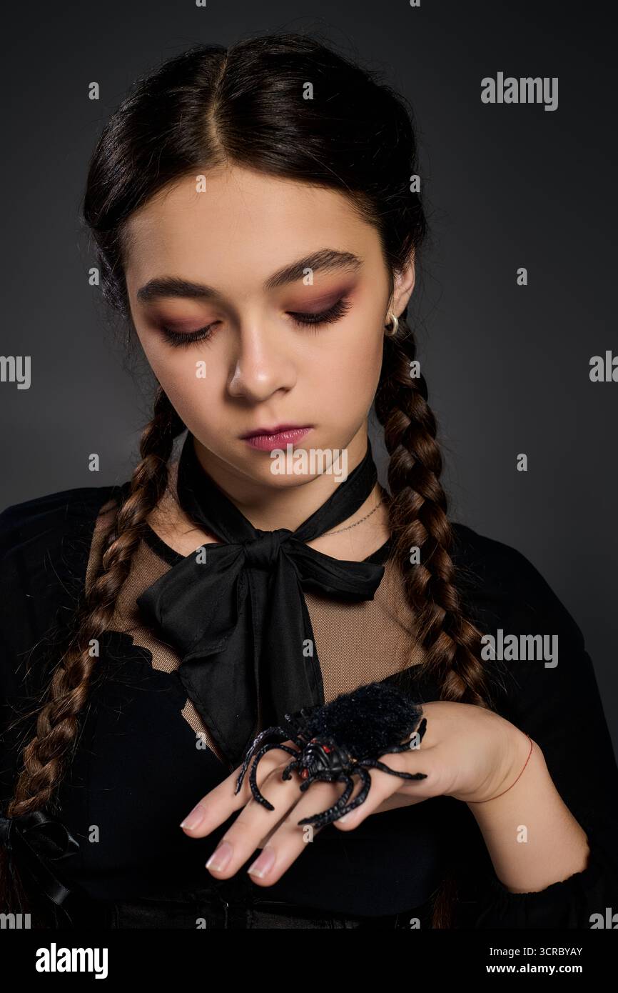 La ragazza con trecce indossa un abito gotico, che incarna un personaggio spaventoso del mercoledì con un ragno Foto Stock