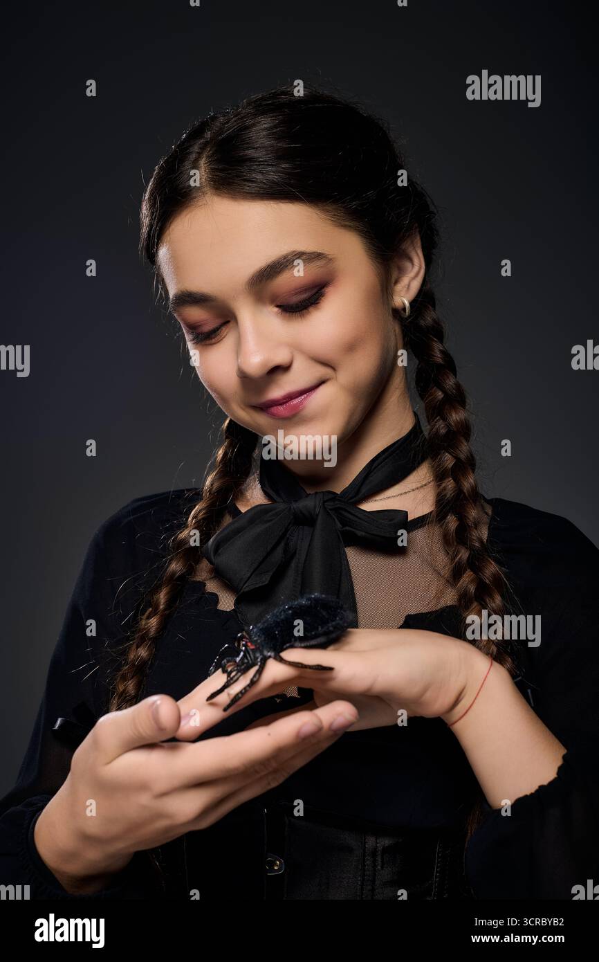 Una ragazza vestita con un costume gotico del mercoledì sorride mentre tiene in mano un ragno spettrale. Foto Stock
