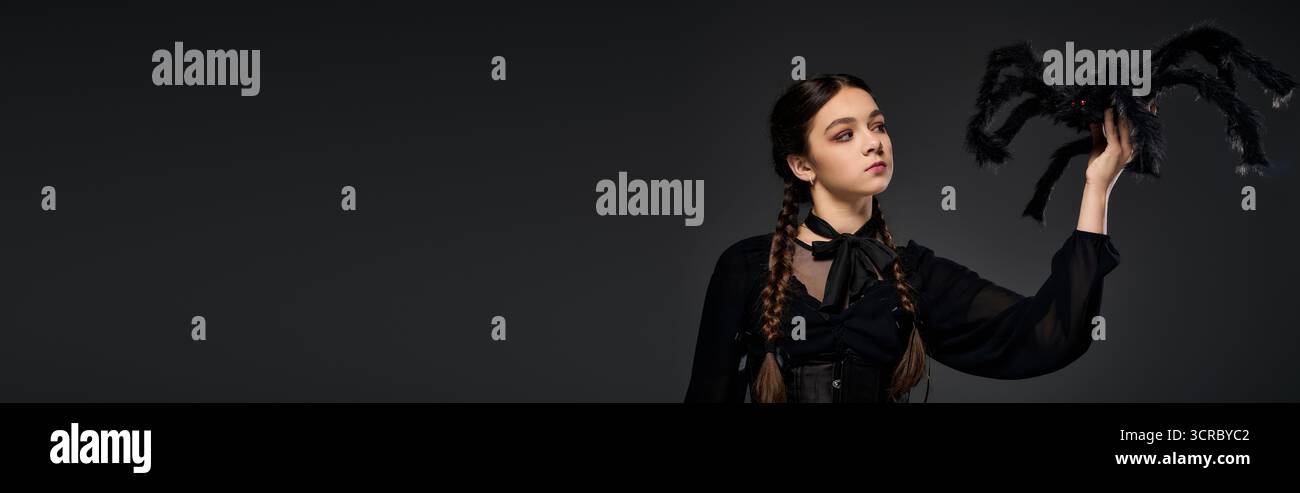 Una ragazza in abito gotico mostra il suo spirito di Halloween con trecce, incarnando un personaggio del mercoledì, uno striscione Foto Stock