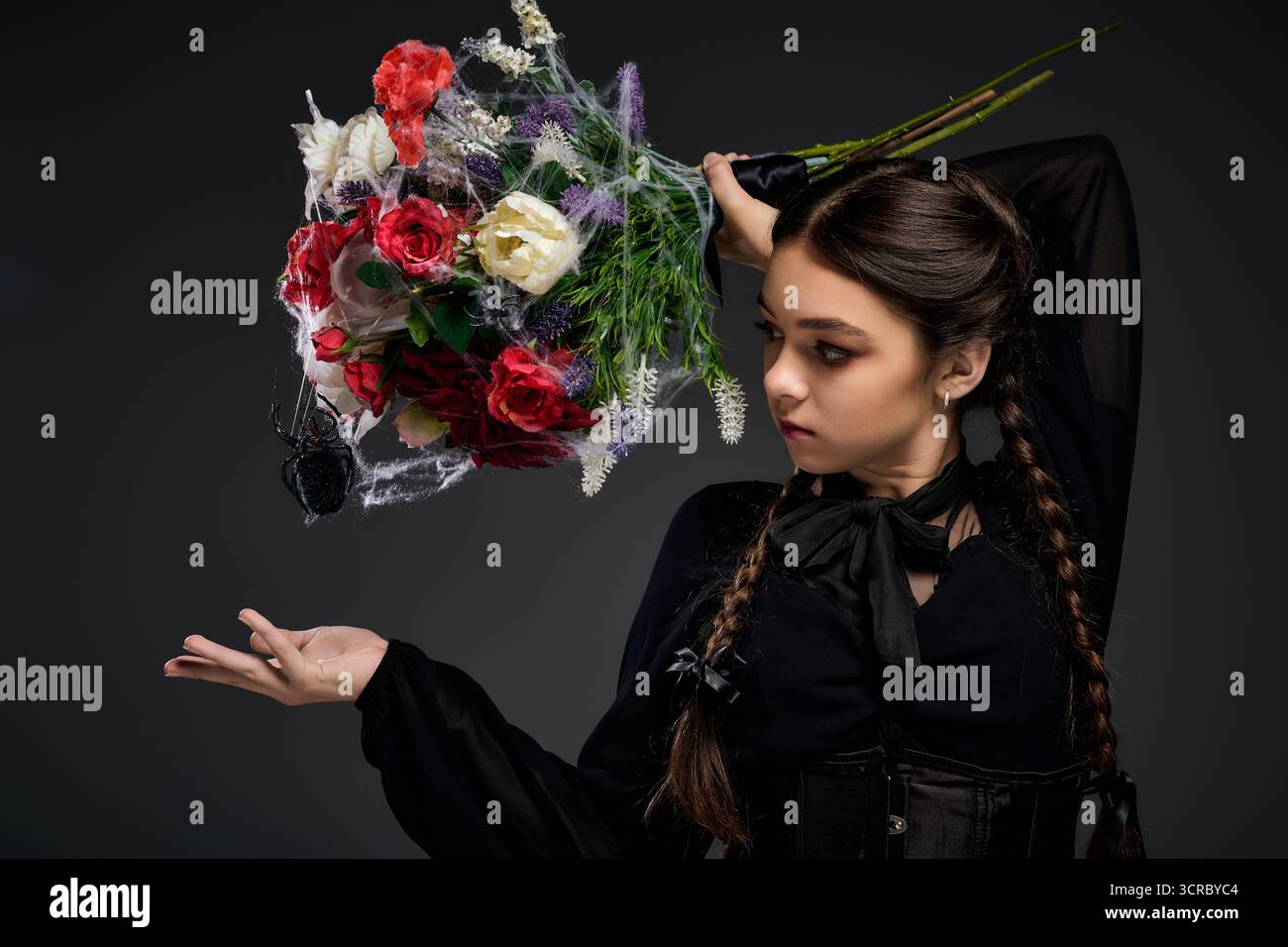 La ragazza con trecce vestita con un abito in stile mercoledì regala un bouquet spettrale durante i festeggiamenti di Halloween. Foto Stock