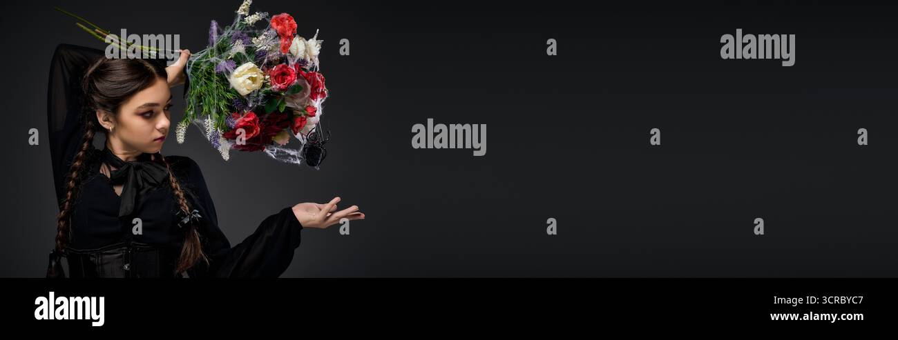Una ragazza con trecce indossa un abito gotico e tiene in mano un spettrale bouquet di fiori per il divertimento di Halloween, striscione Foto Stock