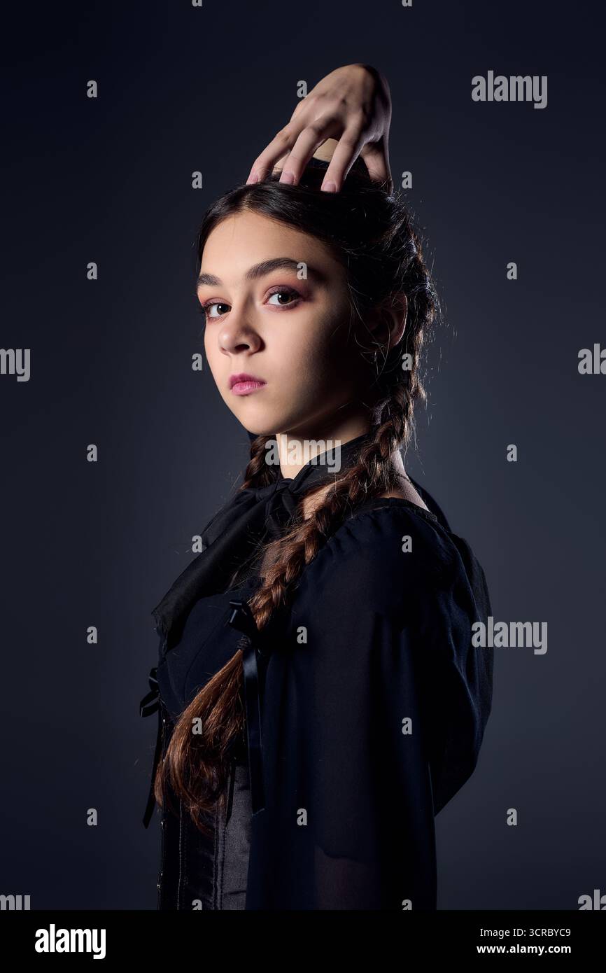 Una ragazza con trecce si posa in un abito gotico scuro del mercoledì, catturando l'essenza di Halloween. Foto Stock
