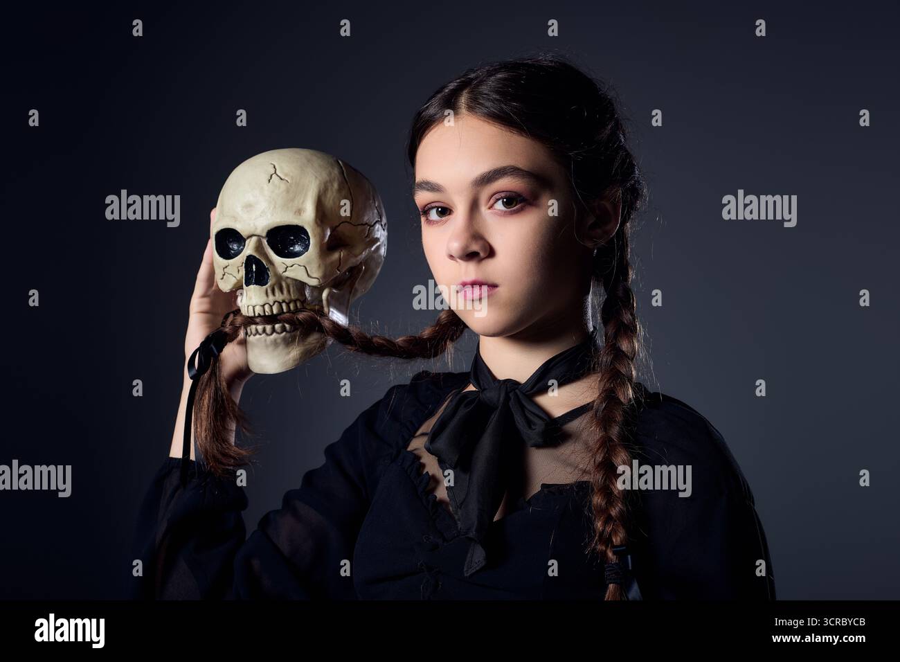 La ragazza con i capelli intrecciati indossa un abito gotico mentre tiene in mano un teschio, mercoledì Foto Stock
