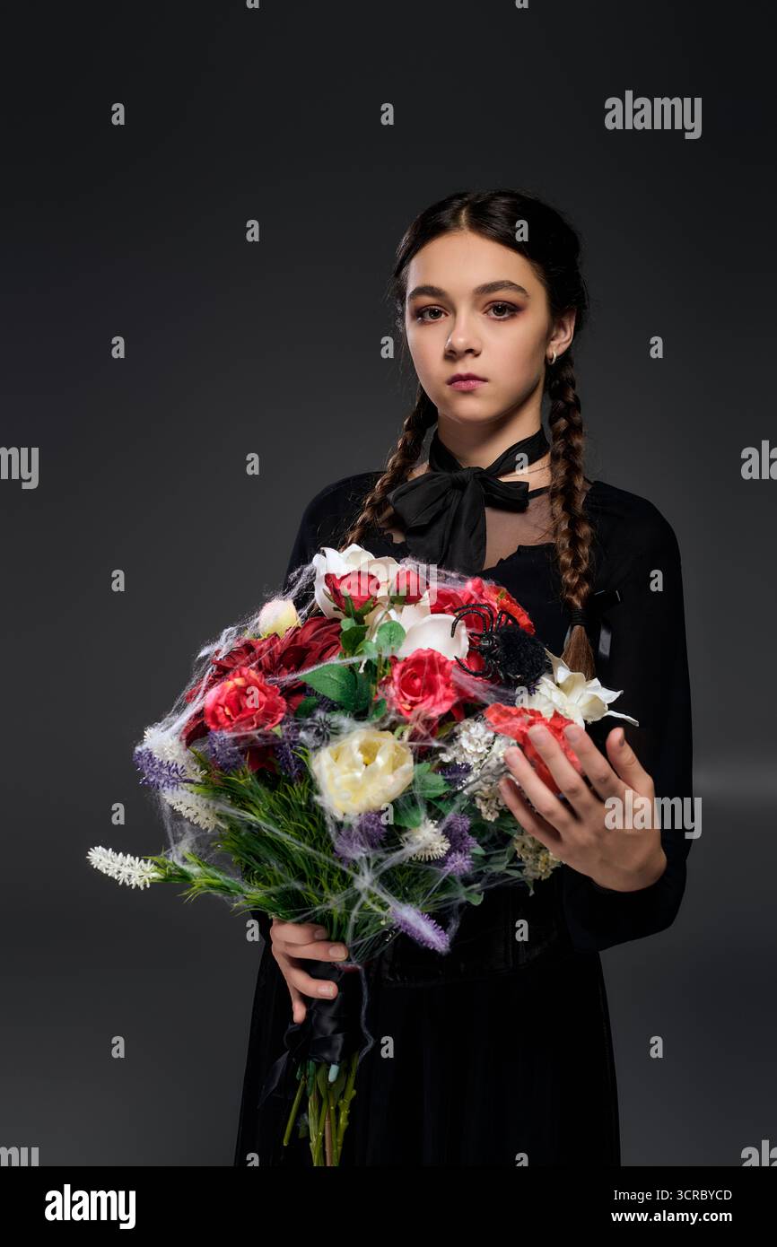 La ragazza con trecce vestita in costume mercoledì regala un bouquet, celebrando la stagione spettrale di ottobre. Foto Stock
