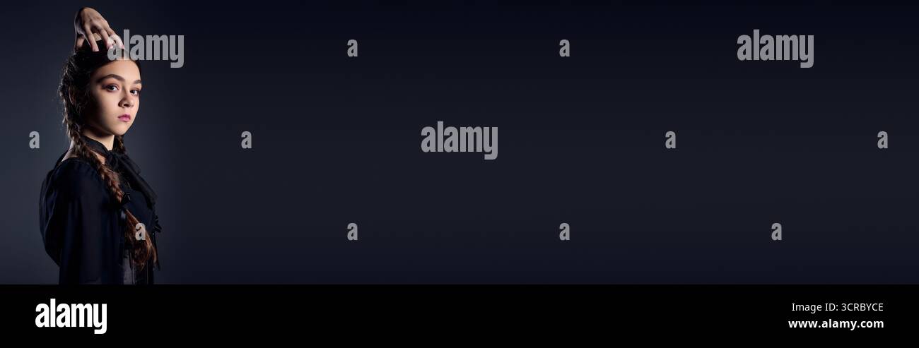 Una ragazza con trecce presenta il suo abito gotico come un personaggio del mercoledì, uno striscione Foto Stock