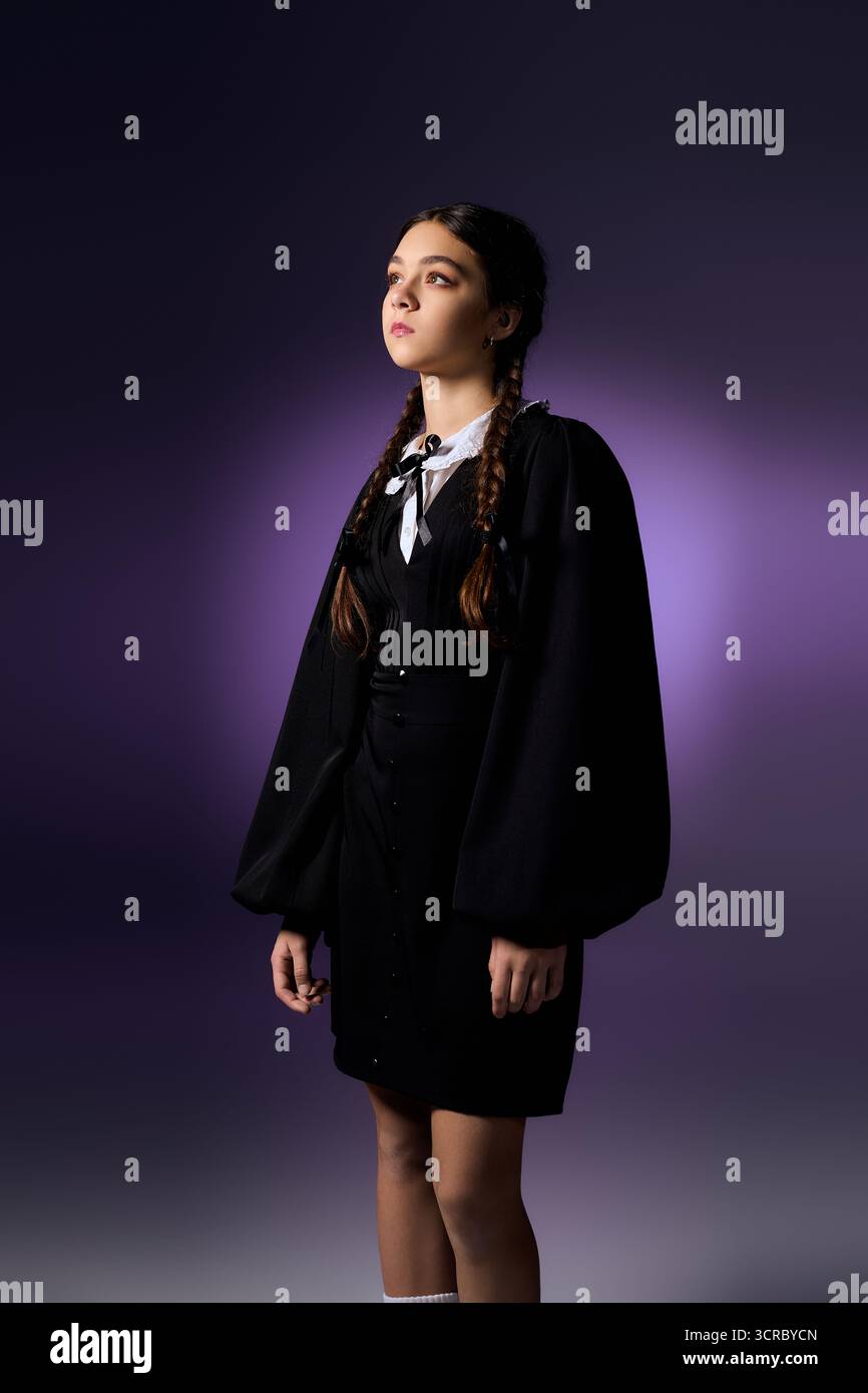 Una ragazza con trecce si erge con fiducia, abbracciando il suo spirito di Halloween in un abito gotico del mercoledì. Foto Stock