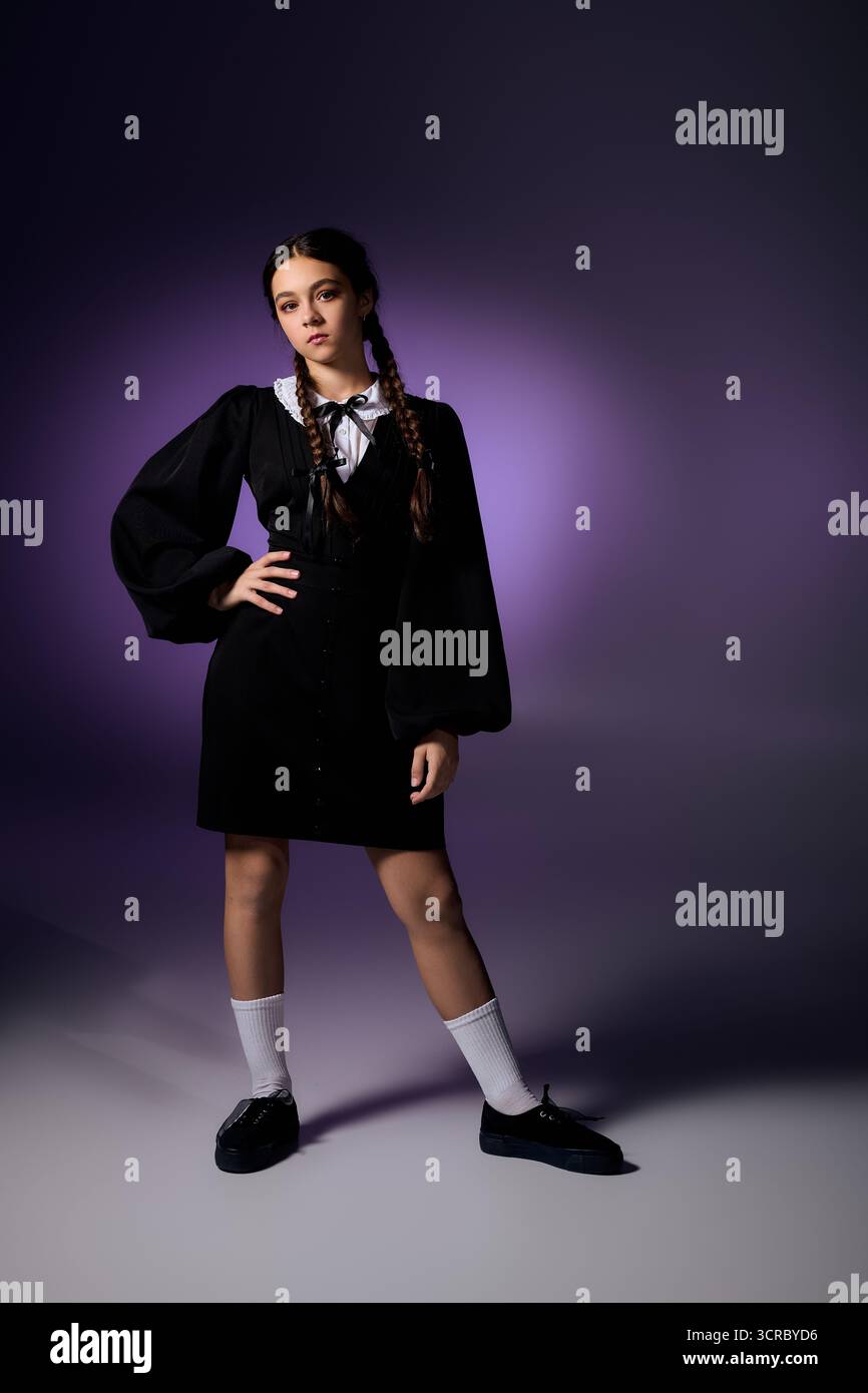Una ragazza con trecce posa in un abito gotico del mercoledì, celebrando Halloween con un'atmosfera spettrale. Foto Stock