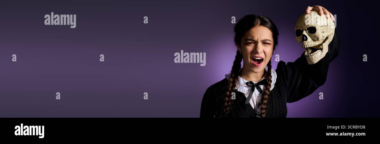 La ragazza con trecce indossa un abito in stile gotico mentre tiene in mano un teschio per il divertimento di Halloween, striscione Foto Stock